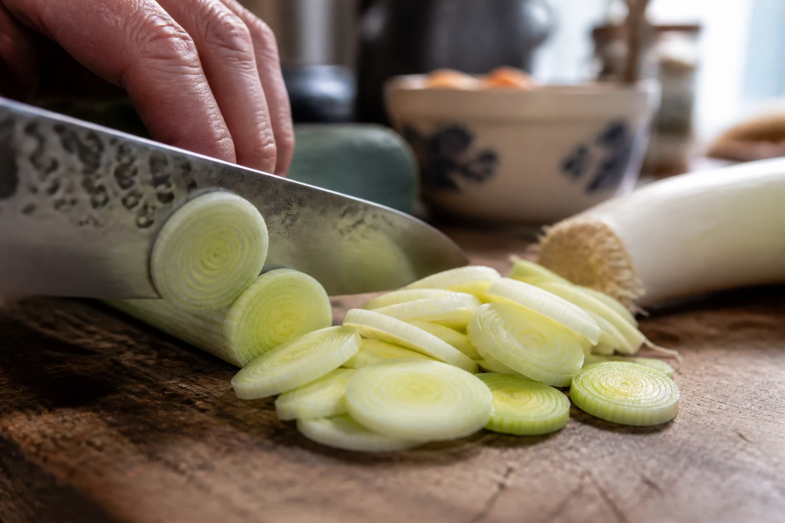 Couper les poireaux en rondelles sur une planche en bois avec un couteau de chef